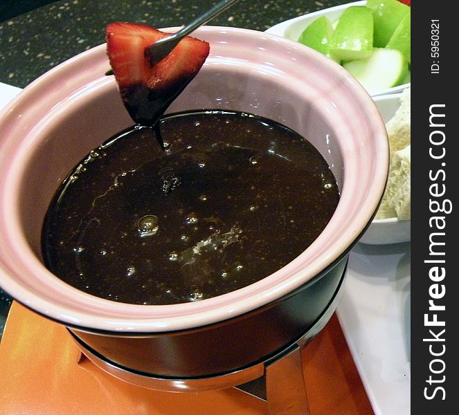 A strawberry dripping chocolate over a fondue pot. A strawberry dripping chocolate over a fondue pot.