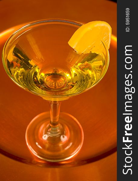 Closeup of a yellow cocktail with a slice of orange on a bronze tray. Closeup of a yellow cocktail with a slice of orange on a bronze tray