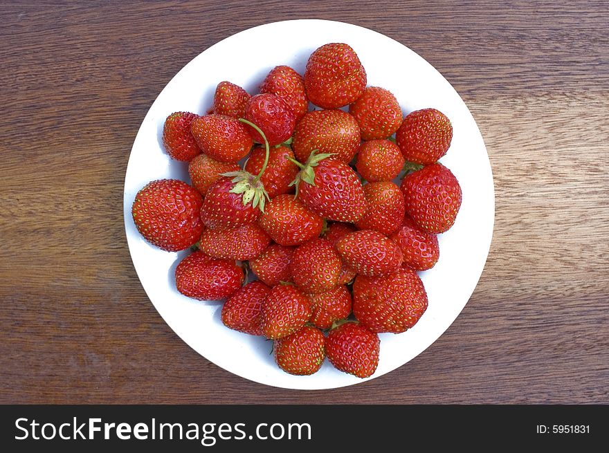 Red, ripe wild strawberry in a white plate on a brown background. Red, ripe wild strawberry in a white plate on a brown background.