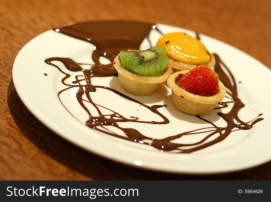 Mixed fruit tarts with chocolate drizzled on plate