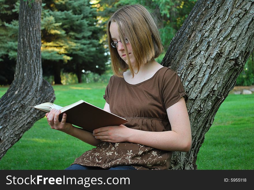 Young girl leaning against a tree reading a book. Young girl leaning against a tree reading a book