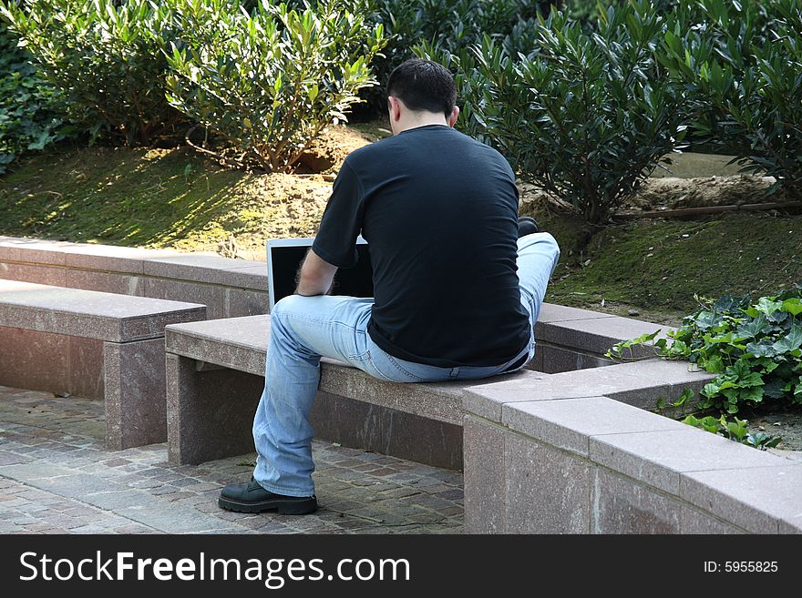 The man sitting on a bench using his laptop. The man sitting on a bench using his laptop