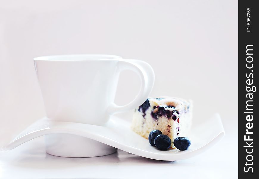 Blueberry cake on a white plate with a matching white cup on a white background