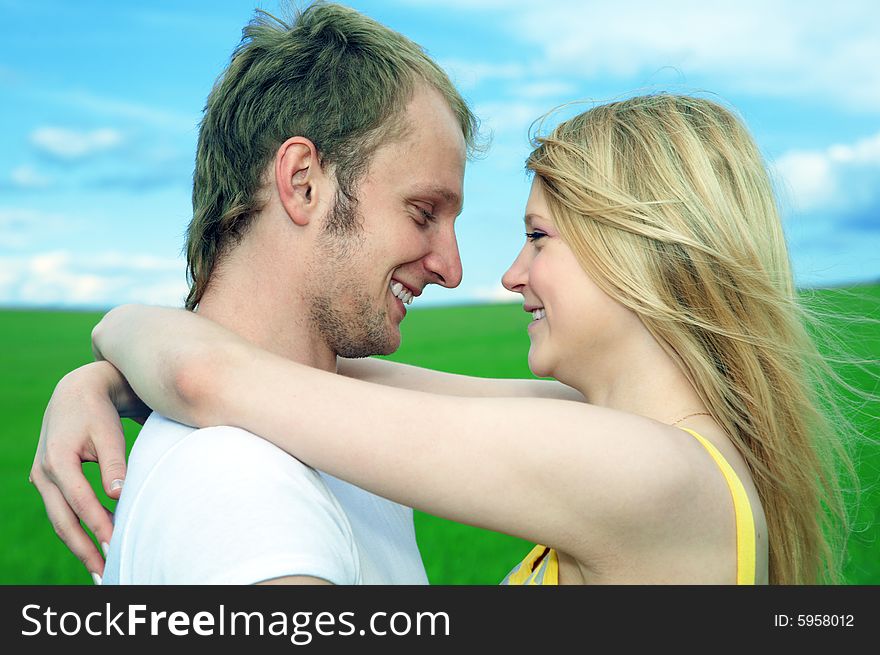 Young love couple embrace in field under blue sky