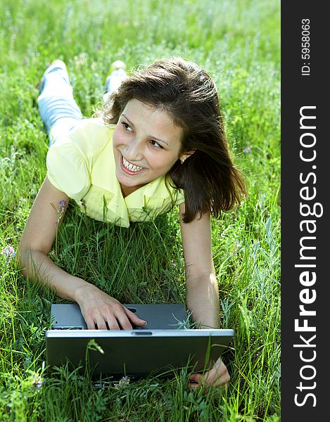 Pretty woman with laptop on the green grass under blue sky