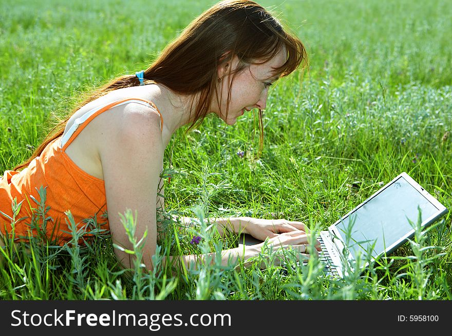 Pretty woman with laptop on the green grass under blue sky