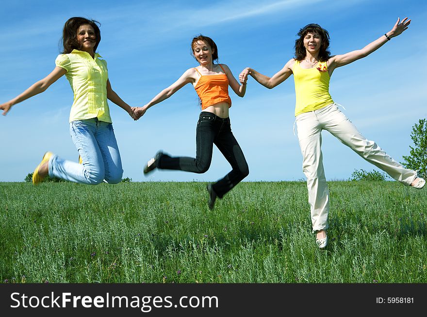 Three girlfriend jump in green field under blue sky