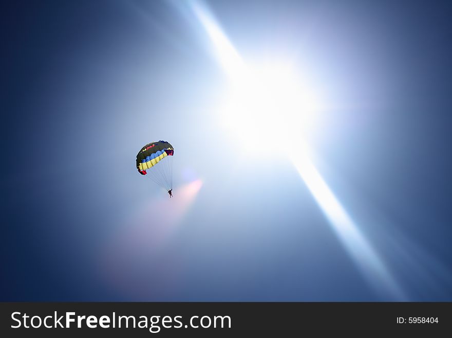 Parachutist at blue sky and bright sun rays