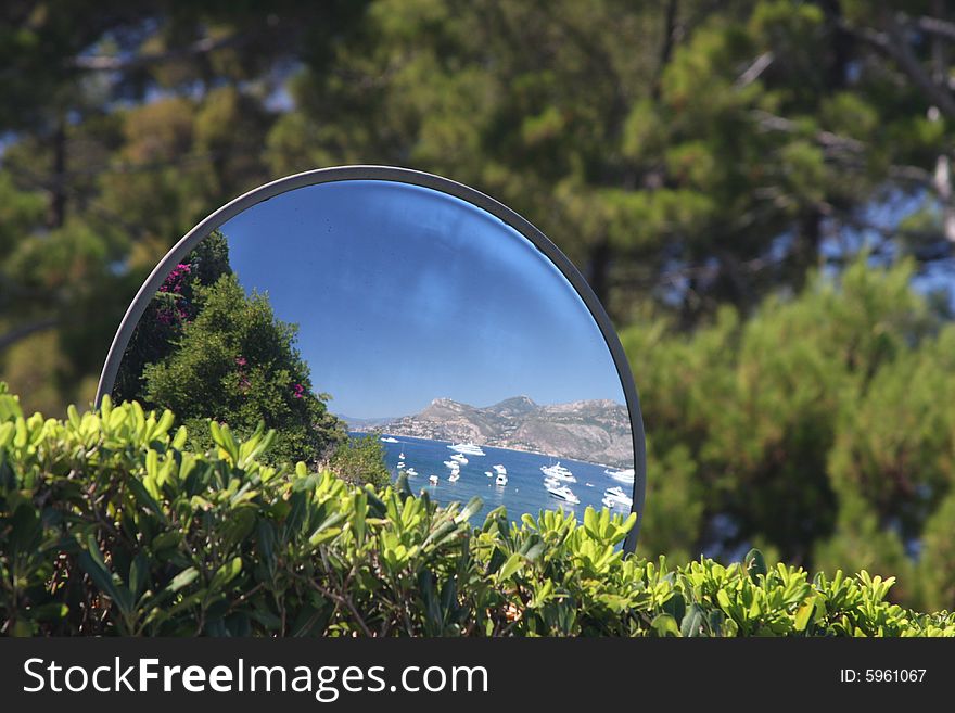 A street mirror reflecting the Mediterranean coast with boats moored. A street mirror reflecting the Mediterranean coast with boats moored