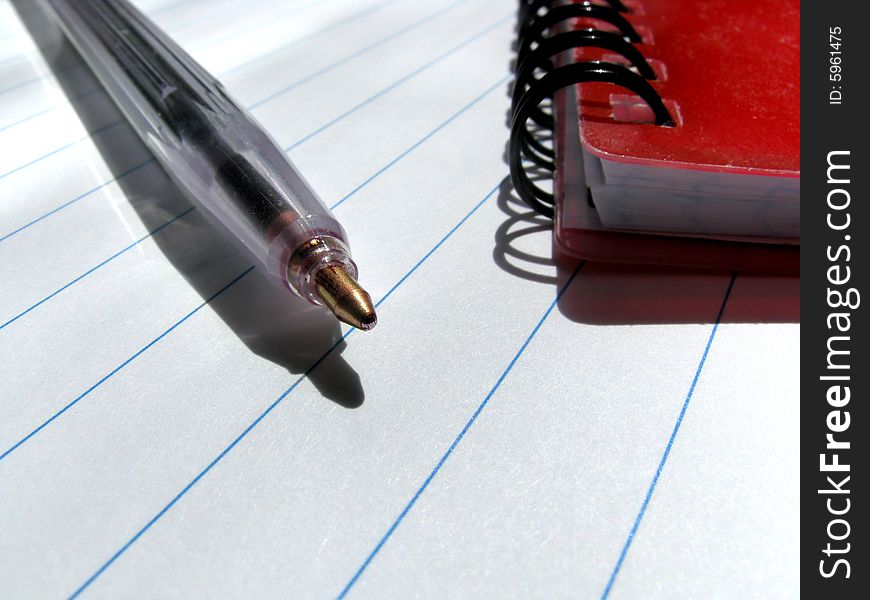 Ballpen and a notebook on a lined surface of a writing-book. Ballpen and a notebook on a lined surface of a writing-book