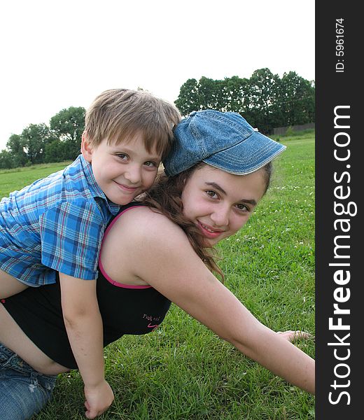 A smiling brother and the sister sit on a grass