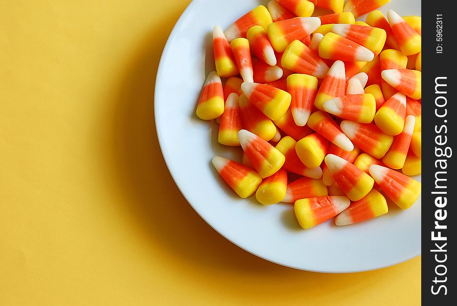 Candy corn on white dish against yellow background