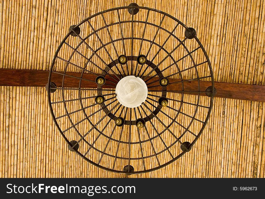 An iron light fixture hanging from a bamboo roof. An iron light fixture hanging from a bamboo roof