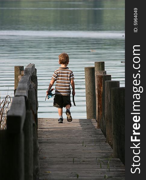 Young boy walking towards a lake on a pier. Young boy walking towards a lake on a pier