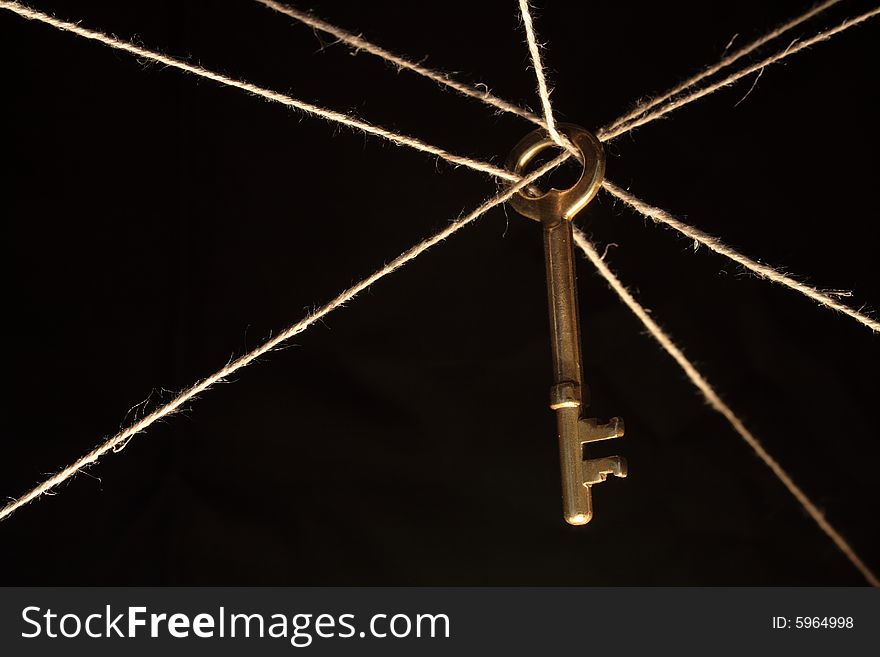 Yellow brass key hanging on ropes on dark background. Yellow brass key hanging on ropes on dark background