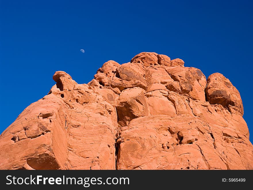 Red rock with moon under blue sky