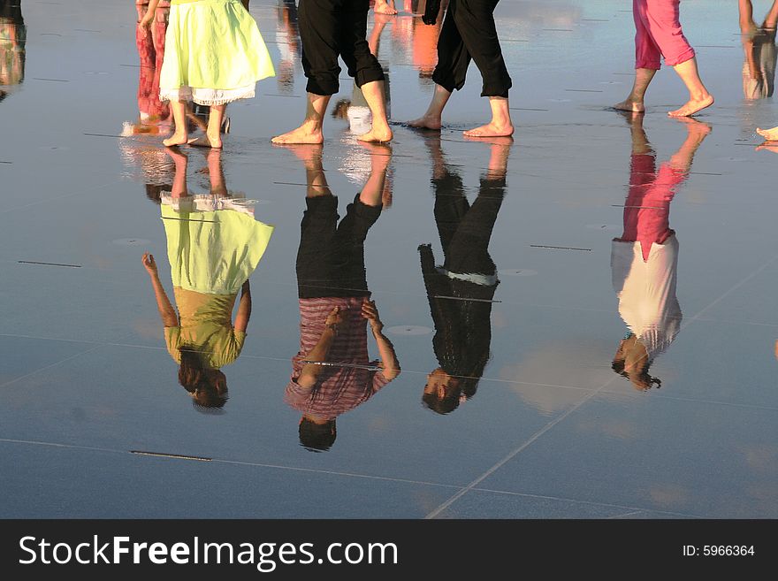 People walking barfoot in a big reflective puddle. People walking barfoot in a big reflective puddle