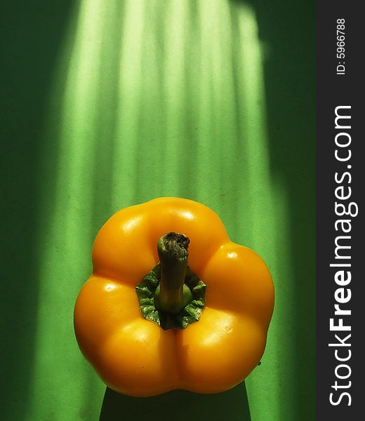 Yellow pepper in solar beams on a green background