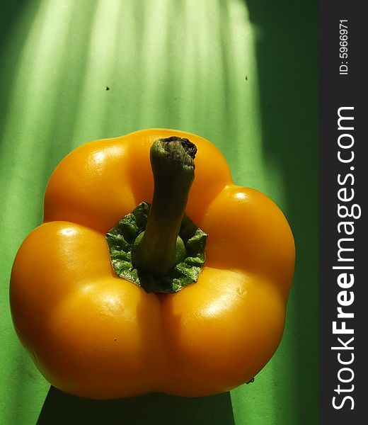 Yellow pepper in solar beams on a green background