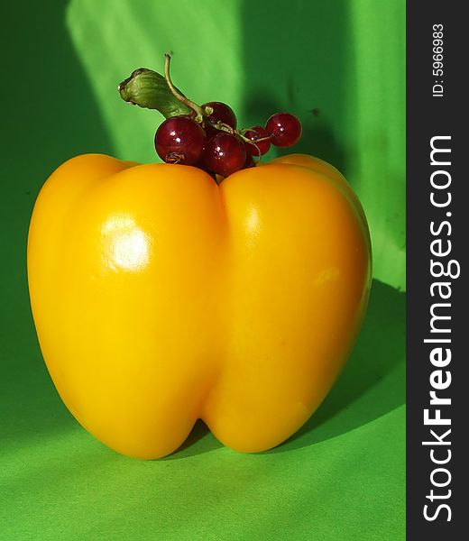 Yellow pepper with a red currant on a green background. Yellow pepper with a red currant on a green background