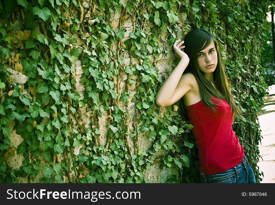 Young woman on wall full of leaves.