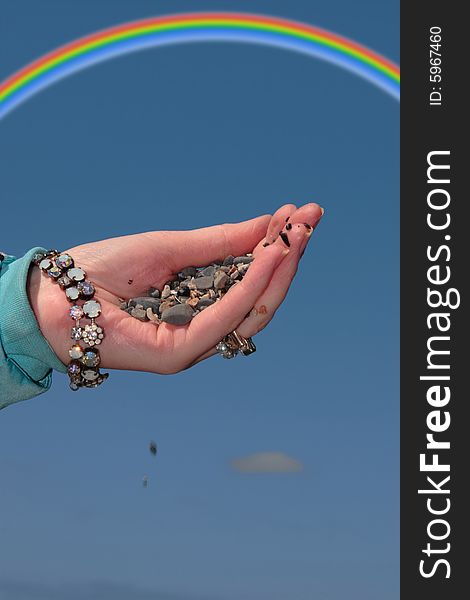 A hand full of earth against a beautiful blue sky with a rainbow in the background. A hand full of earth against a beautiful blue sky with a rainbow in the background