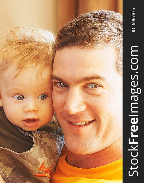 Man holding baby boy close, cheek to cheeck, looking at camera with smile, focus on baby. Man holding baby boy close, cheek to cheeck, looking at camera with smile, focus on baby