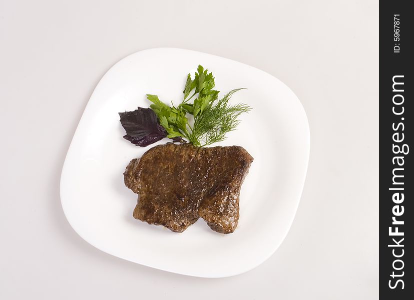 Fried beef steak with parsley, dill and basil on white plate