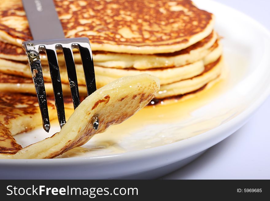 Pile of american pancakes with syrup on a dish and fork piercing a piece. Pile of american pancakes with syrup on a dish and fork piercing a piece.
