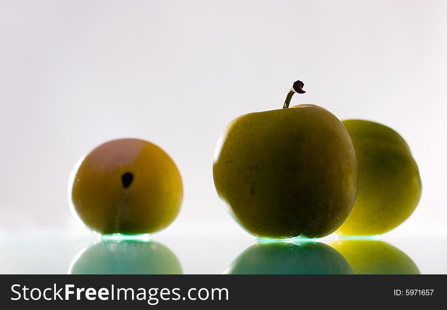 Three plums with reflection over light grey background