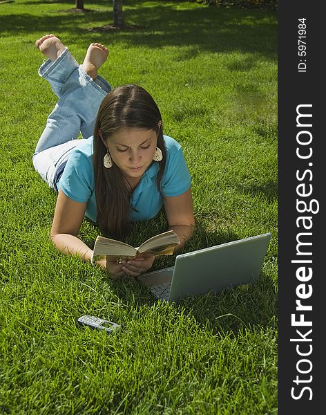 Girl in grass with computer, book, and cell phone. Girl in grass with computer, book, and cell phone
