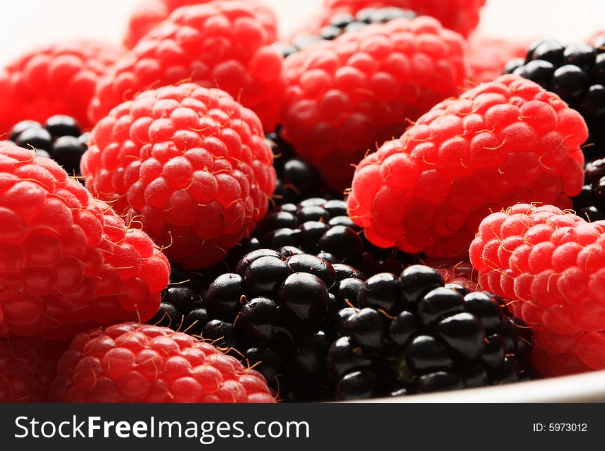 Red raspberries and blackberries in a bowl, lighting from behind to create high contrast. great for concepts of freshness and desserts
