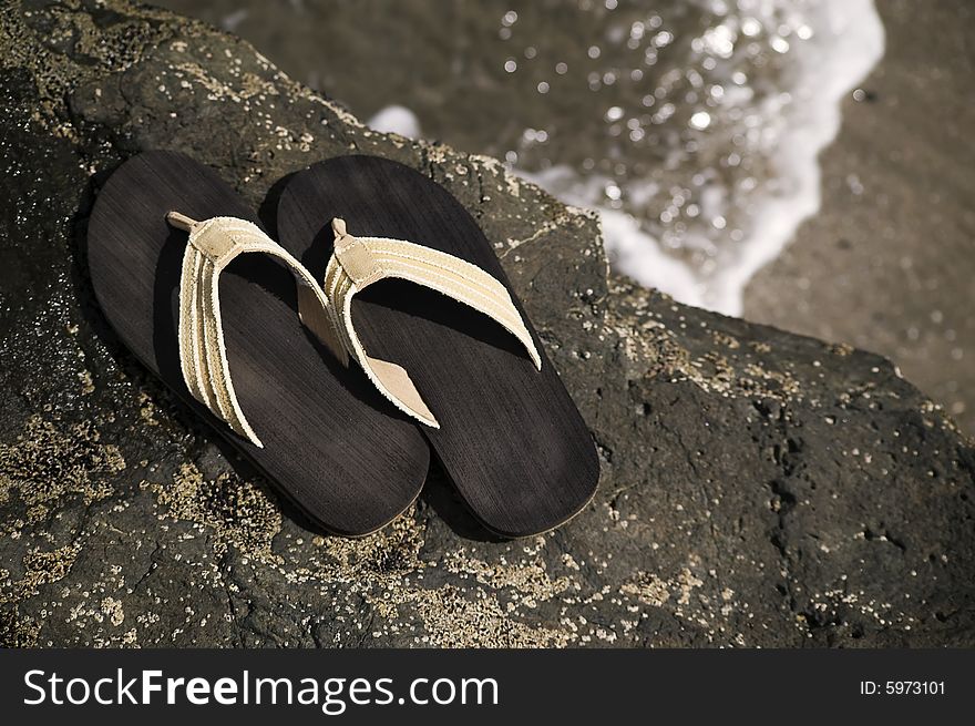 Sandals on a rock with ocean wave in the background. Sandals on a rock with ocean wave in the background