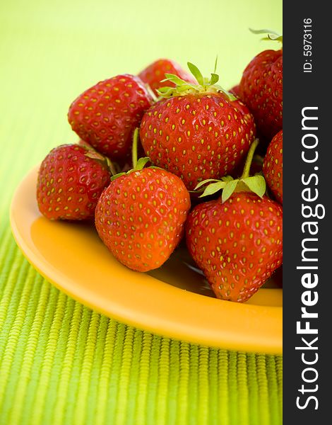 Strawberries piled on the yellow plate over lime background. Strawberries piled on the yellow plate over lime background