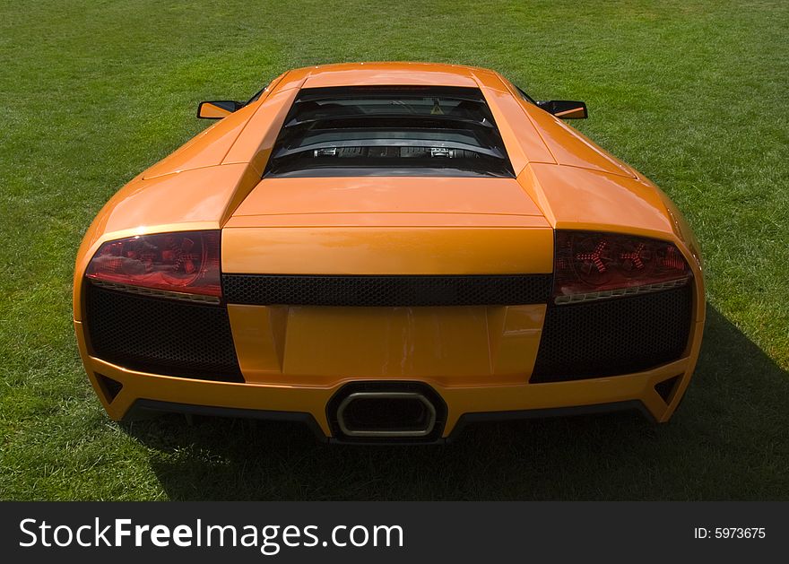 Rear end of Italian super car in metallic orange on lawn. Rear end of Italian super car in metallic orange on lawn
