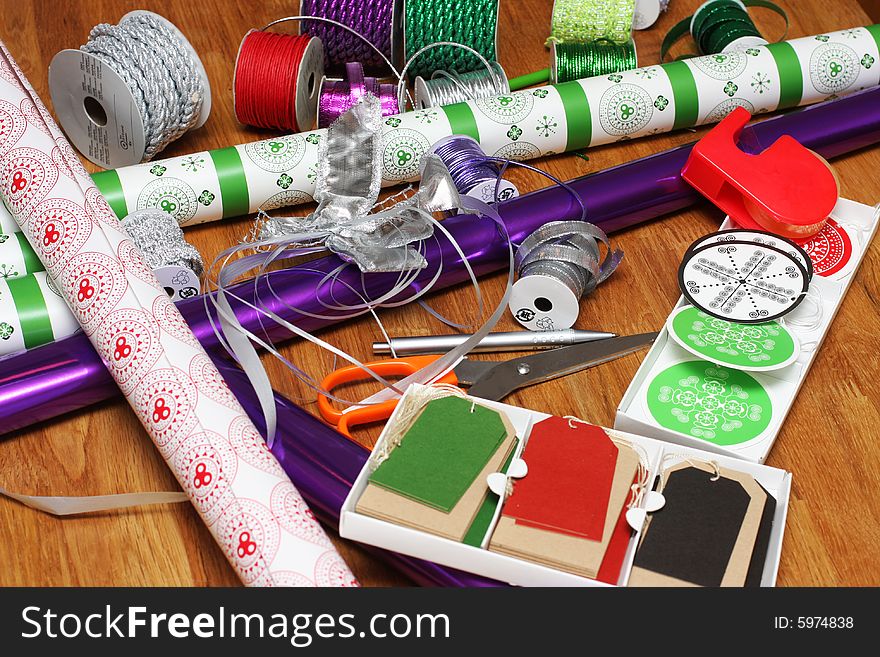 A bunch of wrapping paper, ribbons, label tags and other present wrapping material on an oak table