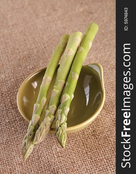 Fresh asparagus in a green bowl on hessian background, shallow DOF
