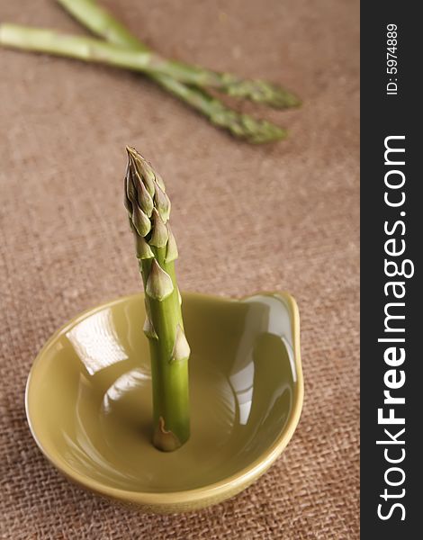 Fresh asparagus spear standing on green plate, on hessian rustic background, shallow DOF