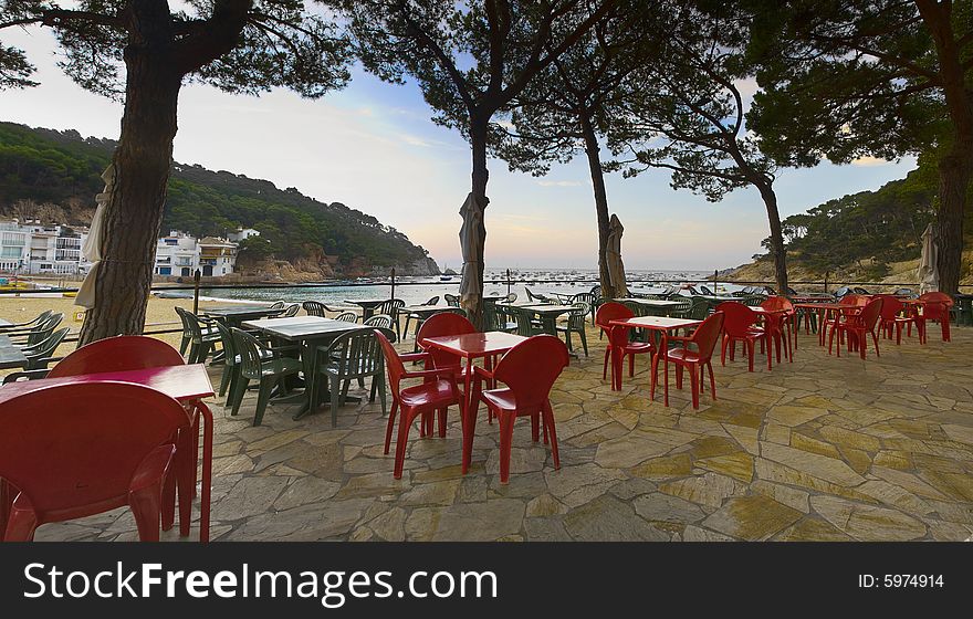 Dawn shot of Restaurant terrace with red and green plastic chairs looking over the beach at Tamariu, Costa Brava, Spain. Dawn shot of Restaurant terrace with red and green plastic chairs looking over the beach at Tamariu, Costa Brava, Spain.