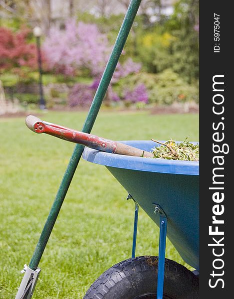 A wheelbarrow filled with grass, a rake balanced upright and a shovel. A wheelbarrow filled with grass, a rake balanced upright and a shovel