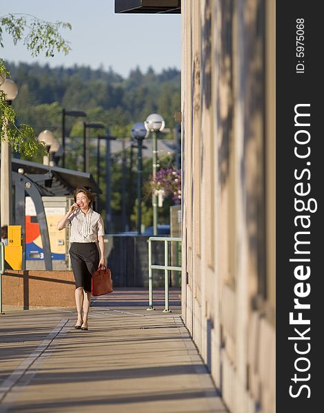 Young woman walks along building while talking on cell phone. Vertically framed photo. Young woman walks along building while talking on cell phone. Vertically framed photo.