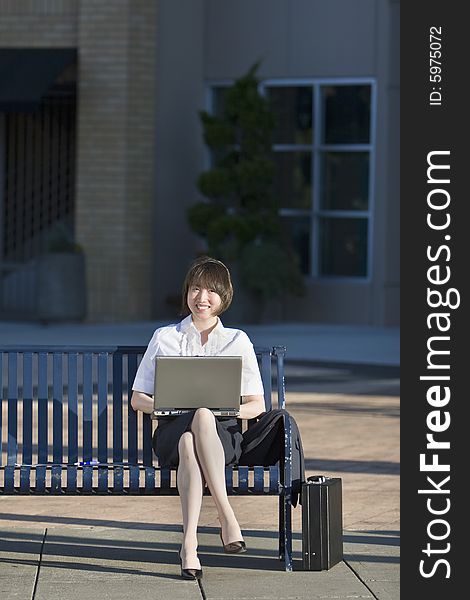 Young woman sits on a bench in front of a building. She is holding her laptop and looks surprised. Vertically framed photo. Young woman sits on a bench in front of a building. She is holding her laptop and looks surprised. Vertically framed photo.