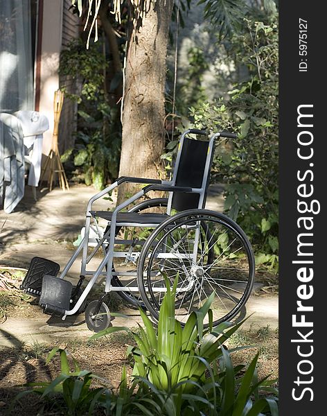 An empty wheelchair is sitting in a garden - Vertically framed shot. An empty wheelchair is sitting in a garden - Vertically framed shot