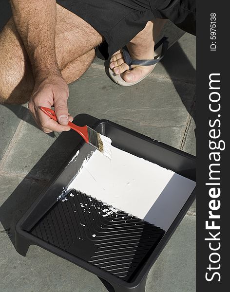 A man is dipping his paint brush into a tray of white paint - Vertically framed shot. A man is dipping his paint brush into a tray of white paint - Vertically framed shot.