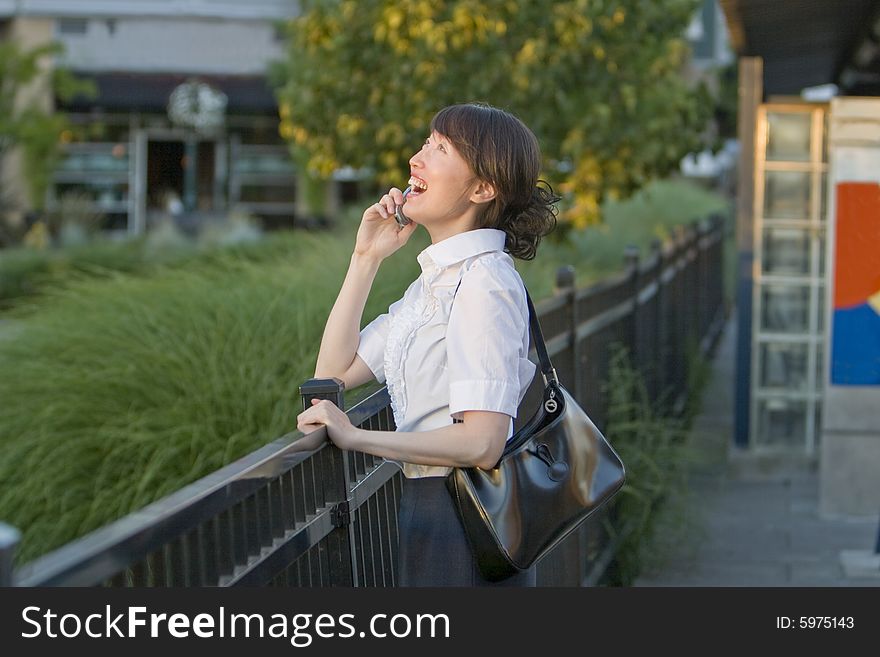 A woman, stands at a railing, holding her cell phone to her ear, laughing heartily. Horizontally framed shot. A woman, stands at a railing, holding her cell phone to her ear, laughing heartily. Horizontally framed shot.