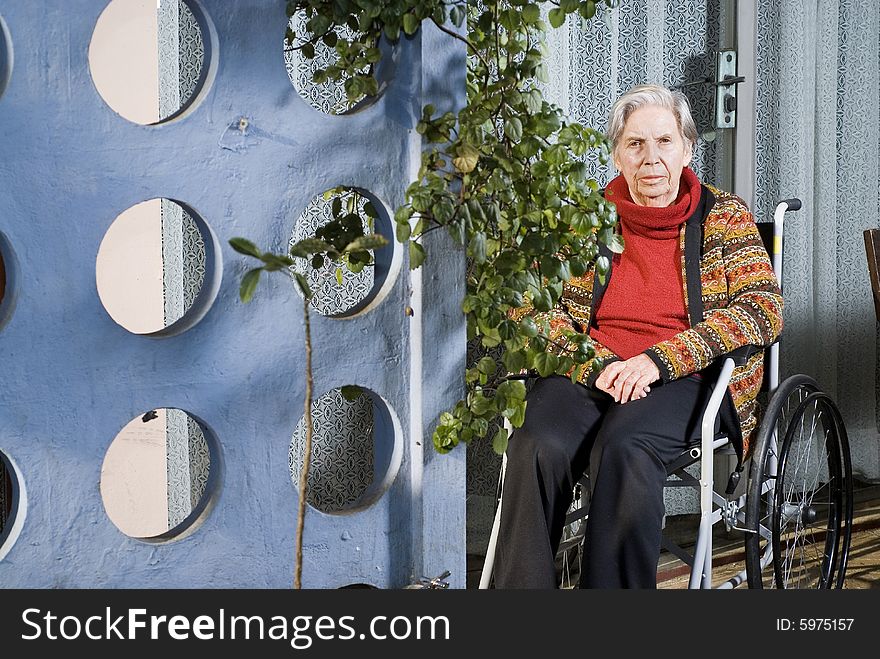 An elderly woman is sitting in a wheelchair in a garden.  She is looking at the camera.  Horizontally framed shot. An elderly woman is sitting in a wheelchair in a garden.  She is looking at the camera.  Horizontally framed shot.