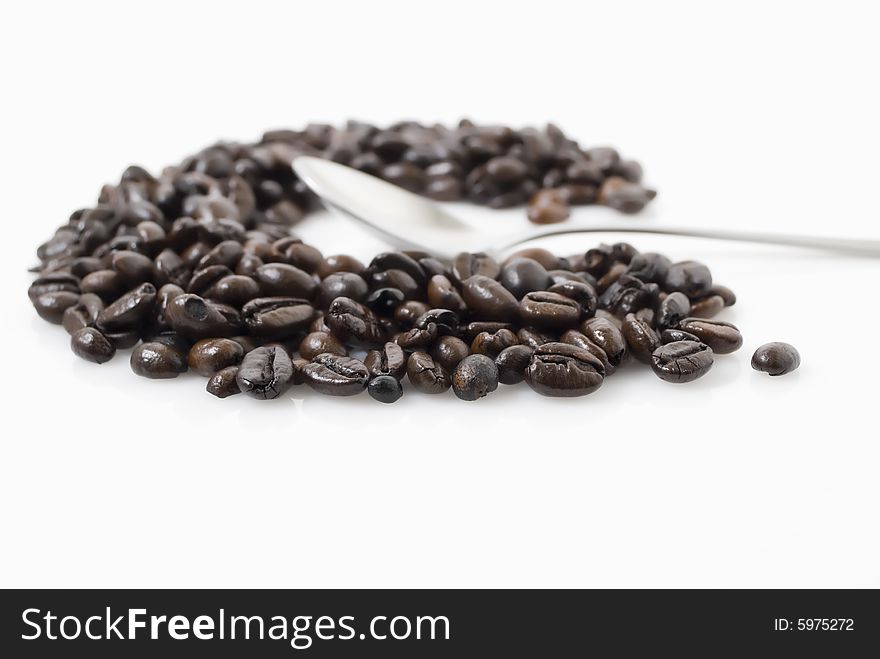 Closeup shot of coffee beans against white background with teaspoon