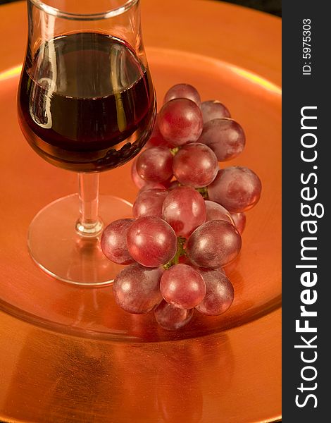 A tasting glass of red wine and grapes on a bronze tray. A tasting glass of red wine and grapes on a bronze tray.