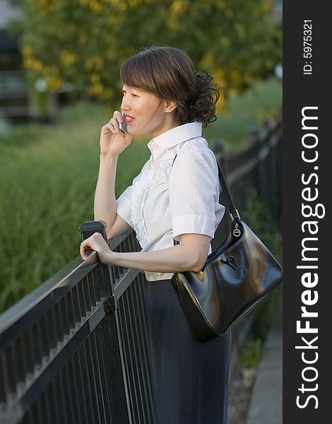 Standing at a rail, a woman talks on her cell phone while smiling. Vertically framed shot. Standing at a rail, a woman talks on her cell phone while smiling. Vertically framed shot.