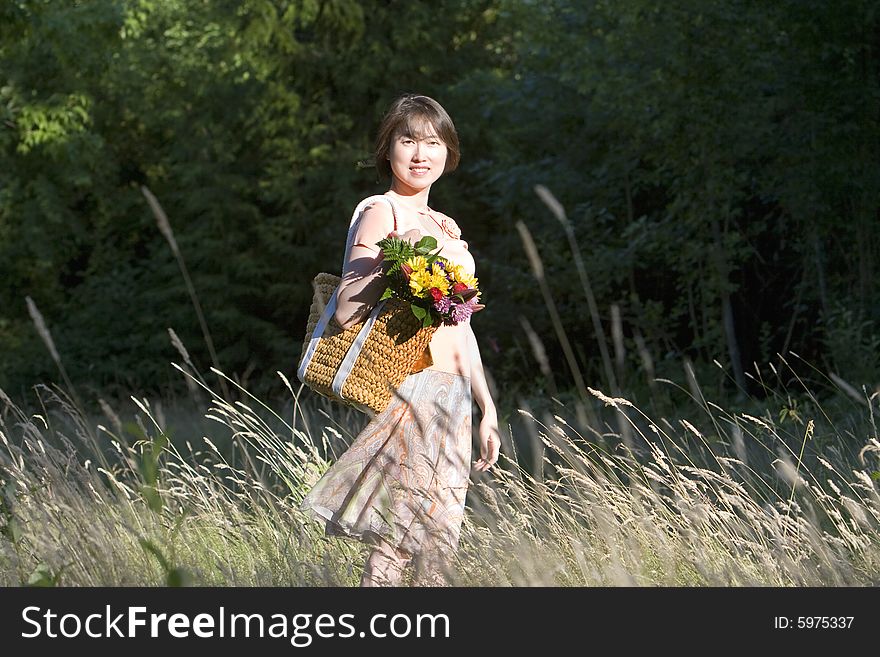 Attractive woman stands in a field while holding a basket containing a bouquet of flowers. She is standing to the side, smiling.  Vertically framed photo. Attractive woman stands in a field while holding a basket containing a bouquet of flowers. She is standing to the side, smiling.  Vertically framed photo.